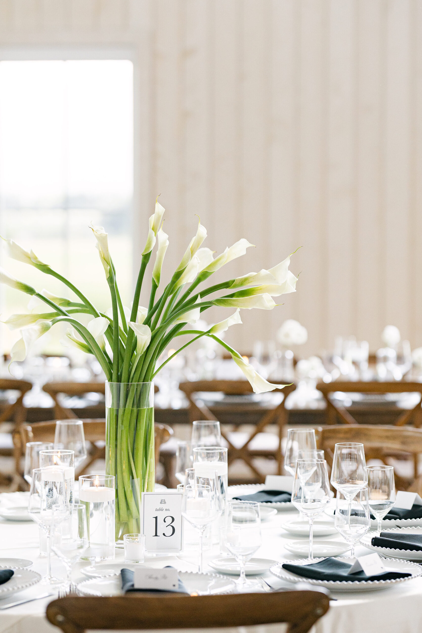Tall glass vase centerpiece with white calla lilies and floating candles on round wedding tables at River Bottoms Ranch in Midway Utah