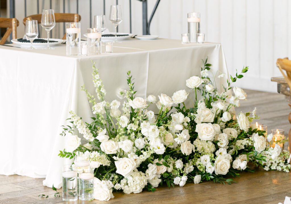 Romantic sweetheart table floral installation with white roses, ranunculus, greenery, and candles at a luxury River Bottoms Ranch wedding in Uta